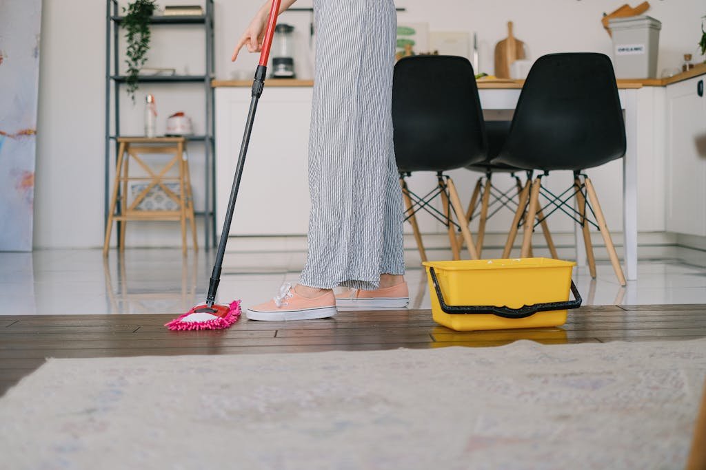 Side view of crop anonymous woman washing parquet with mop against bucket and carpet in house