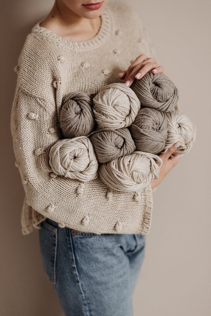 A Person in Beige Knitted Sweater Holding Yarns